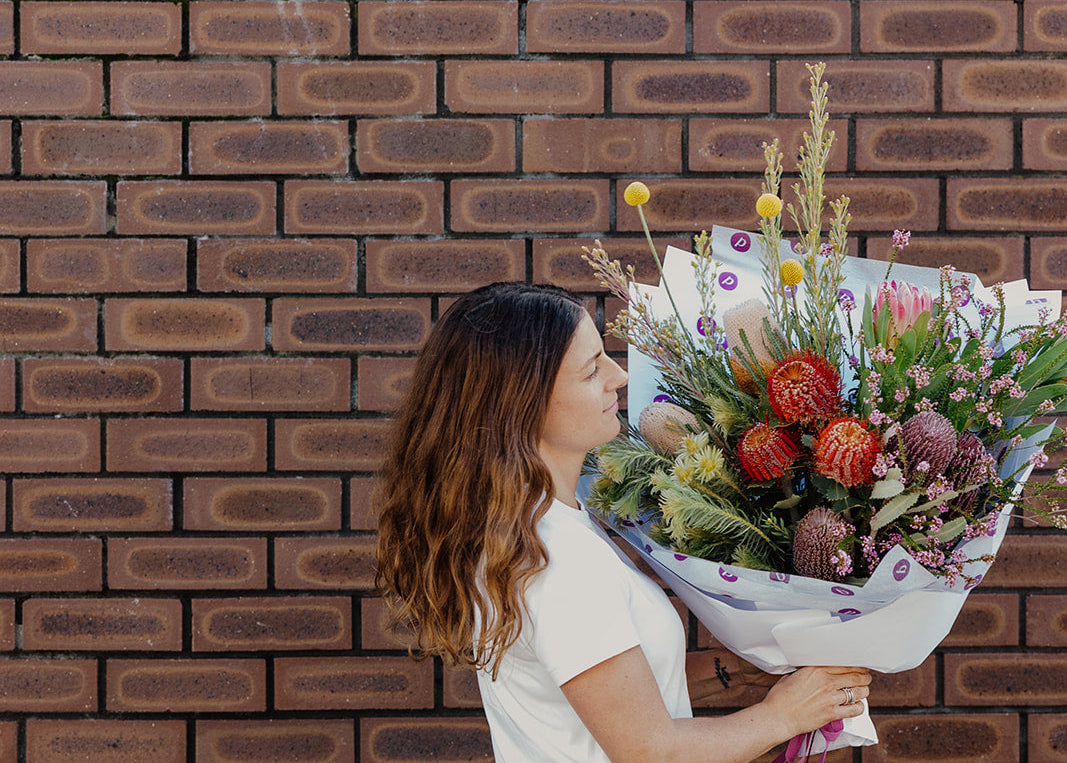 Perth Florist holding a bouquet of flowers against a brick wall